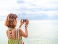 Beautiful asian woman with short hair using smart phone take a photo seascape view