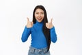 Beautiful asian woman shows thumbs up, enthusiastic cheer up, approve smth, like and recommend, standing over white Royalty Free Stock Photo