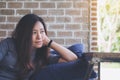 A beautiful Asian woman sit with chin resting on her hands above a blue pillow with feeling happy and relax in cafe Royalty Free Stock Photo