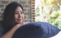 A beautiful Asian woman sit with chin resting on her hands above a blue pillow with feeling happy and relax in cafe Royalty Free Stock Photo