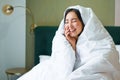 Beautiful asian woman sitting on bed, covered in blankets and duvet, laughing and smiling, enjoying weekend in bedroom Royalty Free Stock Photo