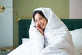 Beautiful asian woman sitting on bed, covered in blankets and duvet, laughing and smiling, enjoying weekend in bedroom Royalty Free Stock Photo