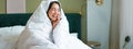 Beautiful asian woman sitting on bed, covered in blankets and duvet, laughing and smiling, enjoying weekend in bedroom Royalty Free Stock Photo