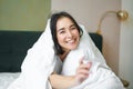 Beautiful asian woman sitting on bed, covered with white duvet, smiling, enjoying happy weekend morning, laughing at Royalty Free Stock Photo