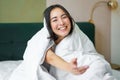 Beautiful asian woman sitting on bed, covered with white duvet, smiling, enjoying happy weekend morning, laughing at Royalty Free Stock Photo