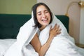 Beautiful asian woman sitting on bed, covered with white duvet, smiling, enjoying happy weekend morning, laughing at Royalty Free Stock Photo