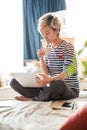 Beautiful Asian woman sitting on bed & working from home on laptop