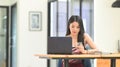 A beautiful Asian woman is sitting in front of a computer laptop at the wooden working desk Royalty Free Stock Photo
