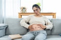 Beautiful Asian woman sitting on sofa in living room touching belly A pregnant single mother lays down the book you are reading.