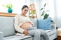 Beautiful Asian woman sitting on the sofa in the living room touching the belly. single mother who is pregnant puts down Royalty Free Stock Photo