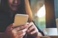 A beautiful Asian woman with smiley face holding and using smart phone with coffee cup on wooden table Royalty Free Stock Photo