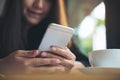 A beautiful Asian woman with smiley face holding and using smart phone with coffee cup on wooden table Royalty Free Stock Photo