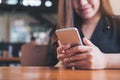 A beautiful Asian woman with smiley face holding and using smart phone with coffee cup on wooden table Royalty Free Stock Photo