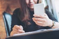 A beautiful Asian woman with smiley face holding and using smart phone with magazines on wooden table Royalty Free Stock Photo