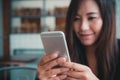 A beautiful Asian woman with smiley face holding and using smart phone in modern cafe Royalty Free Stock Photo