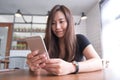 A beautiful Asian woman with smiley face holding and using smart phone in modern cafe Royalty Free Stock Photo