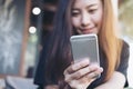 A beautiful Asian woman with smiley face holding and using smart phone in modern cafe Royalty Free Stock Photo