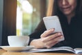 A beautiful Asian woman with smiley face holding and using smart phone while reading magazines with coffee cup on wooden table