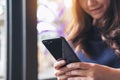 A beautiful Asian woman with smiley face using and looking at a black smart phone Royalty Free Stock Photo