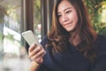 A beautiful Asian woman with smiley face using and looking at smart phone in modern cafe with green vertical garden Royalty Free Stock Photo