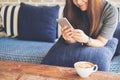 A beautiful Asian woman with smiley face using and looking at smart phone sitting on sofa with white latte coffee cup Royalty Free Stock Photo