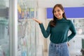 beautiful asian woman smiling with hand gesture offering something near cell phone accessories display case Royalty Free Stock Photo