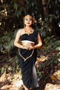 Beautiful Asian woman standing in a black dress while wearing a golden crown and golden chain inside the forest Royalty Free Stock Photo