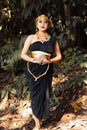 Beautiful Asian woman standing in a black dress while wearing a golden crown and golden chain inside the forest Royalty Free Stock Photo