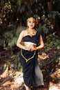 Beautiful Asian woman standing in a black dress while wearing a golden crown and golden chain inside the forest Royalty Free Stock Photo