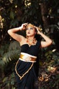 Beautiful Asian woman standing in a black dress while wearing a golden crown and golden chain inside the forest Royalty Free Stock Photo