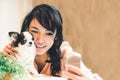 Beautiful Asian woman taking selfie with cute Chihuahua dog at home, with copy space. Lovely human and pet friendship