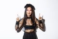 Beautiful asian woman in undead widow costume, wearing black lace dress for halloween, pointing fingers up and smiling