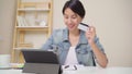 Beautiful Asian woman using tablet buying online shopping by credit card while wear casual sitting on desk in living room at home
