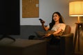 Beautiful asian woman watching television sitting on a comfortable sofa with the remote control in her hand. Royalty Free Stock Photo