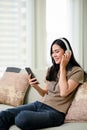 Beautiful Asian woman wearing headphones, listening to music, using her smartphone Royalty Free Stock Photo