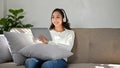 Beautiful Asian woman wearing headphones, using tablet while relaxing on her sofa Royalty Free Stock Photo