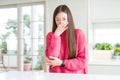 Beautiful Asian woman wearing pink sweater on white table smelling something stinky and disgusting, intolerable smell, holding Royalty Free Stock Photo