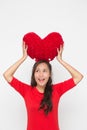 Beautiful Asian woman wearing small Santa hat and wearing red dress holding red heart shape pillow on white background Royalty Free Stock Photo