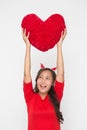 Beautiful Asian woman wearing small Santa hat and wearing red dress holding red heart shape pillow on white background Royalty Free Stock Photo