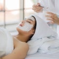 Beautiful asian woman wearing spa style white robe doing brush a facial mask herb white cream to on customer`s face for well face Royalty Free Stock Photo