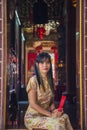 Beautiful Asian woman wearing traditional yellow cheongsam qipao dress holding red fan sitting and looking to a camera at a wooden Royalty Free Stock Photo