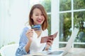 A beautiful Asian woman wearing a white shirt with a credit card comes out of her wallet smiling happily in front of her laptop Royalty Free Stock Photo