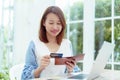 A beautiful Asian woman wearing a white shirt with a credit card comes out of her wallet smiling happily in front of her laptop Royalty Free Stock Photo