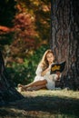 Beautiful asian woman in white dress sit under the tree  writing and thinking in the park with autumn leaves Royalty Free Stock Photo