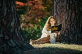 Beautiful asian woman in white dress sit under the tree  writing and thinking in the park with autumn leaves Royalty Free Stock Photo