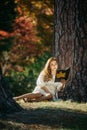 Beautiful asian woman in white dress sit under the tree  writing and thinking in the park with autumn leaves Royalty Free Stock Photo