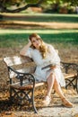 Beautiful asian woman in white dress sit under the tree  writing and thinking in the park with autumn leaves Royalty Free Stock Photo