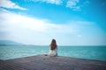 A beautiful asian woman on white dress sitting and looking at the sea and blue sky on wooden balcony Royalty Free Stock Photo