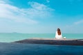 A beautiful asian woman on white dress sitting and looking at the sea and blue sky on wooden balcony Royalty Free Stock Photo
