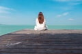 A beautiful asian woman on white dress sitting and looking at the sea and blue sky on wooden balcony Royalty Free Stock Photo